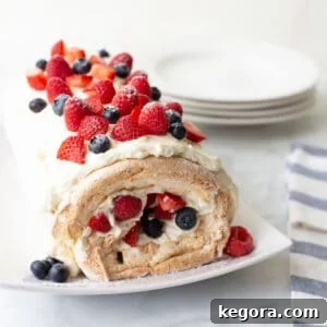 An exquisite gluten-free angel food cake roll, elegantly arranged on a white serving dish and garnished with a medley of vibrant fresh berries, perfect as a stunning holiday dessert.