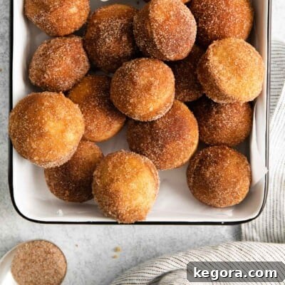 A side view of golden-brown gluten-free French breakfast puffs, generously coated in cinnamon sugar, arranged invitingly in a casserole dish, perfect for a morning treat.