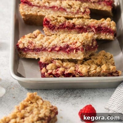 Beautifully stacked gluten-free raspberry crumb bars in a baking dish, featuring a golden oat topping and a luscious red raspberry filling, ready for serving.