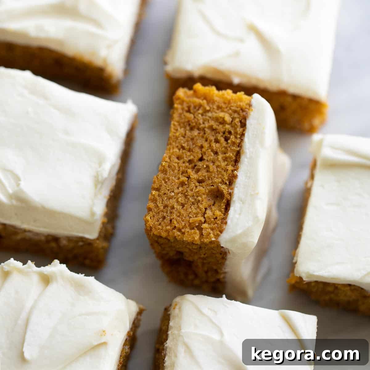 Rows of perfectly cut gluten-free pumpkin bars with cream cheese frosting on a marble slab, ready for sharing.