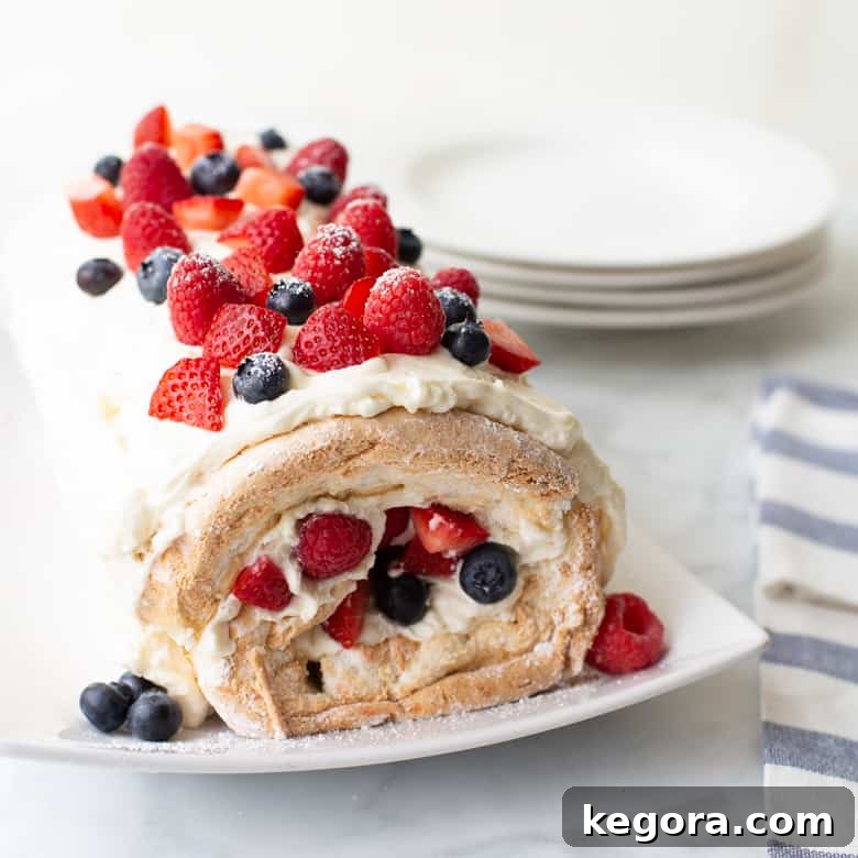A festive gluten-free angel food cake roll adorned with fresh berries, perfect for a Fourth of July dessert.