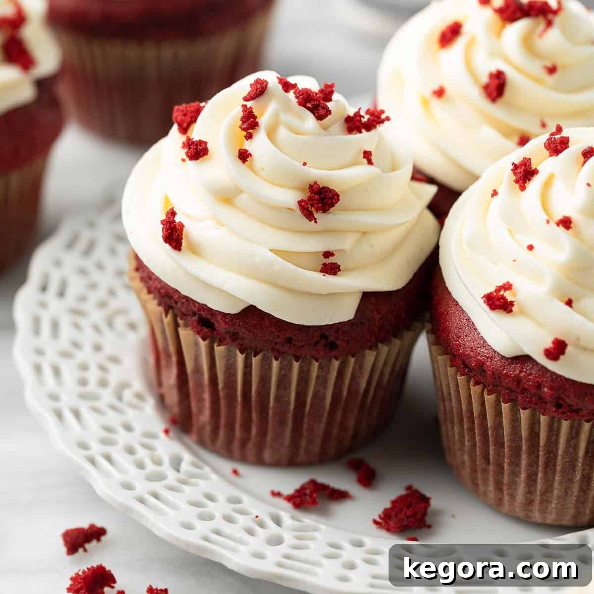 Beautifully frosted gluten-free red velvet cupcakes on a white plate, garnished with cake crumbs.