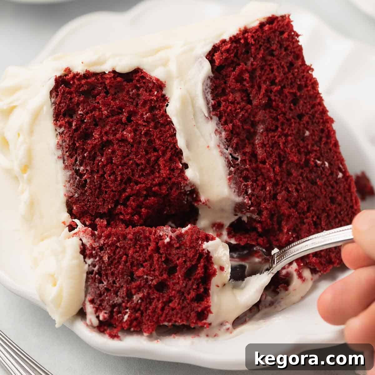 A fork taking a delicious bite out of a slice of rich gluten-free red velvet cake, revealing its moist layers.