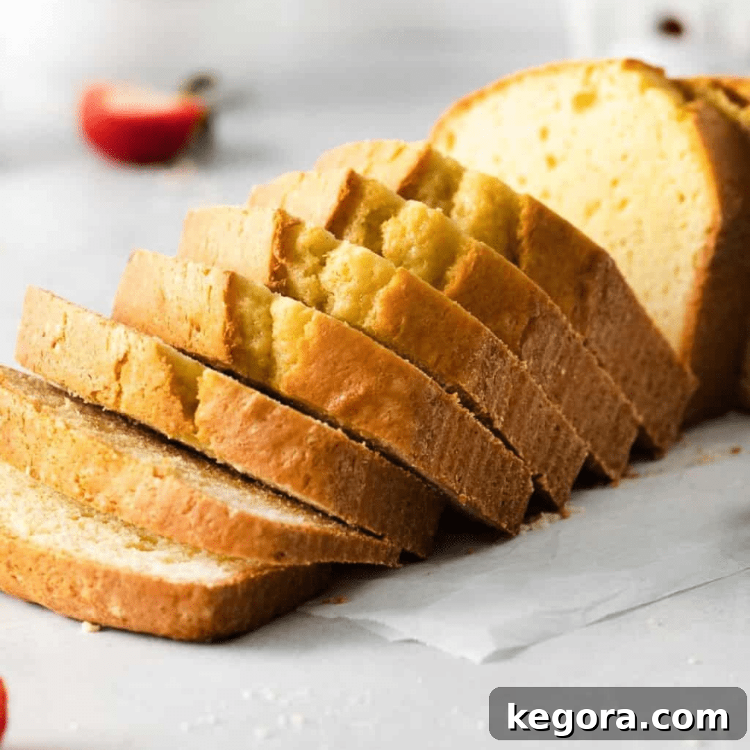 A beautifully sliced loaf of golden gluten-free pound cake displayed on a rustic countertop.