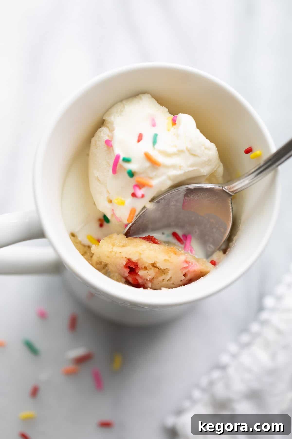 A freshly baked gluten-free mug cake with a spoon on a kitchen countertop, ready to be enjoyed.