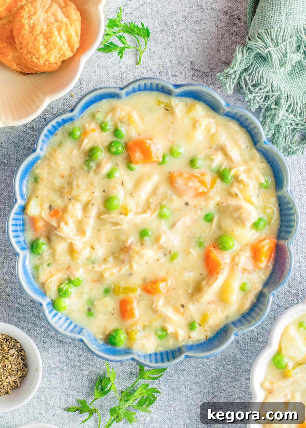 A blue bowl filled with creamy Instant Pot Chicken Pot Pie Soup, garnished with fresh herbs, sitting on a rustic wooden surface.