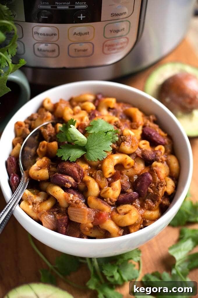 Hearty Instant Pot Chili Mac 2 Chili Mac in a white bowl with spoon on wooden board, ready to be served