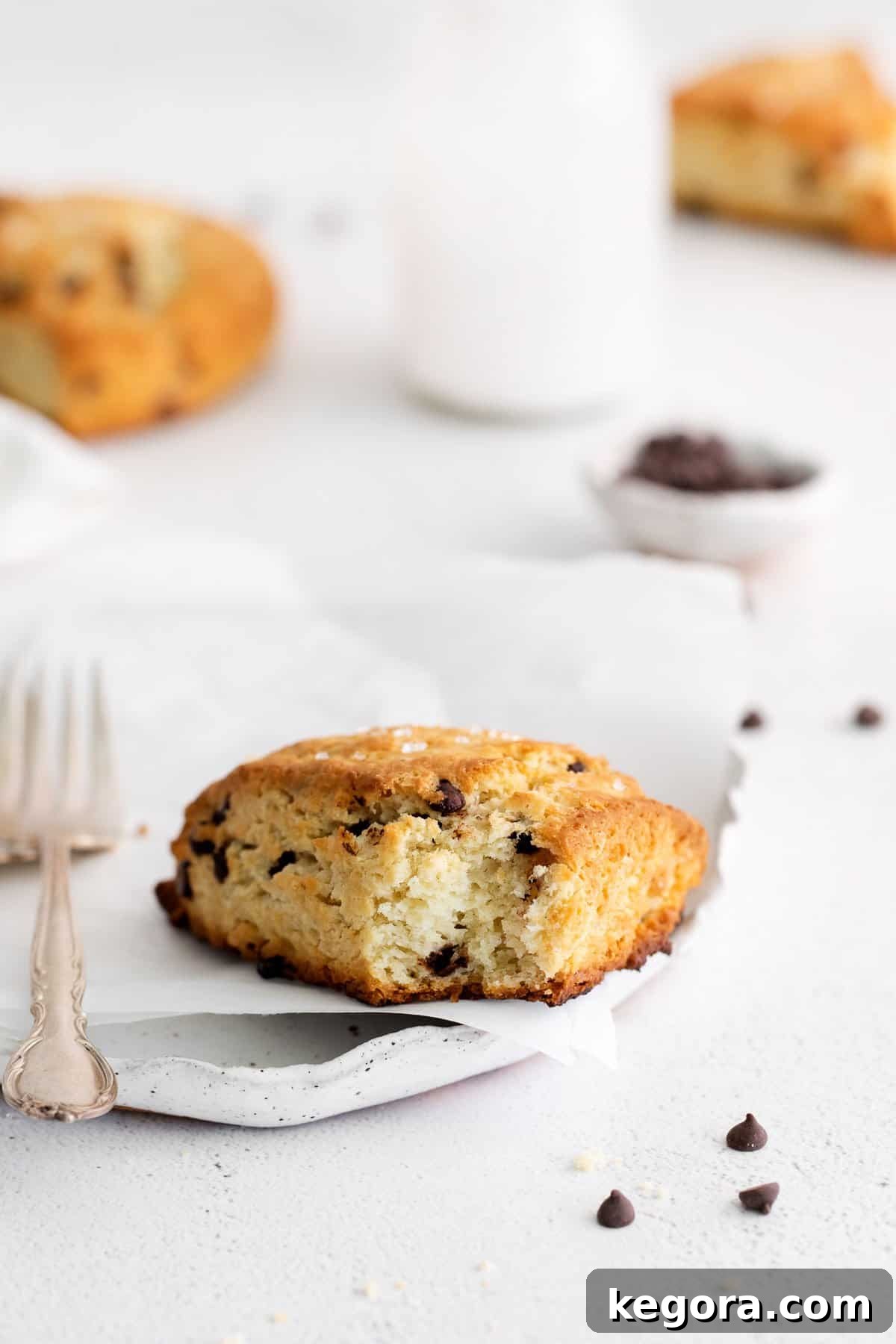 A gluten-free chocolate chip scone on a plate with a fork beside it