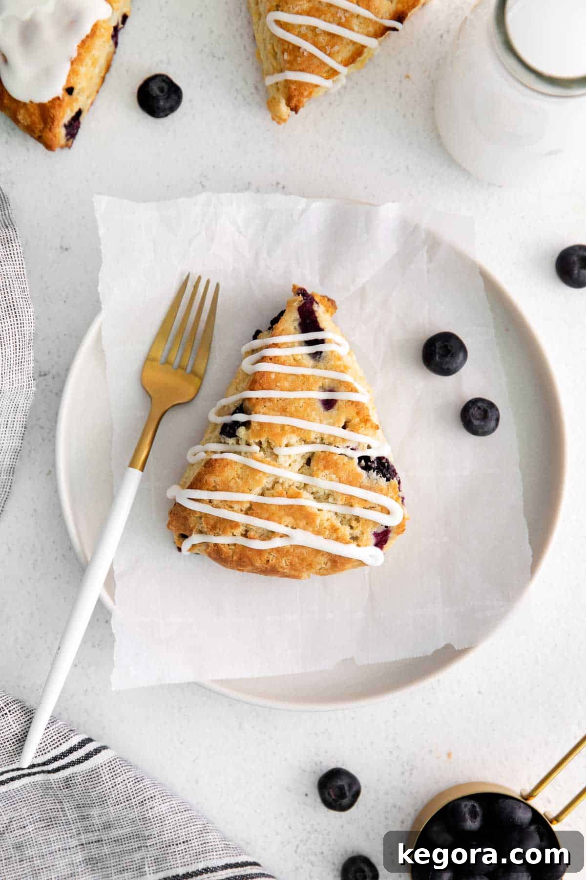 An overhead view of a perfectly baked gluten-free blueberry scone on a white plate, ready to be enjoyed.