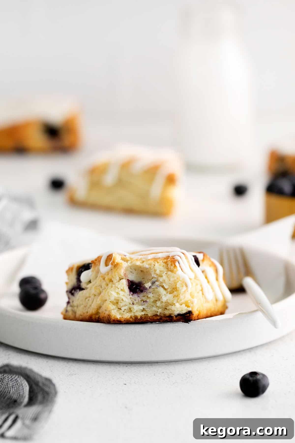 A single gluten-free blueberry scone on a plate with one bite taken, showcasing its flaky interior and blueberries.