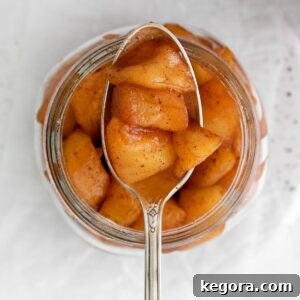 A spoonful of tender apple compote held over a glass jar filled with the same delicious compote.