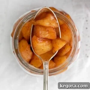 A spoonful of chunky apple compote held over a jar of more compote.