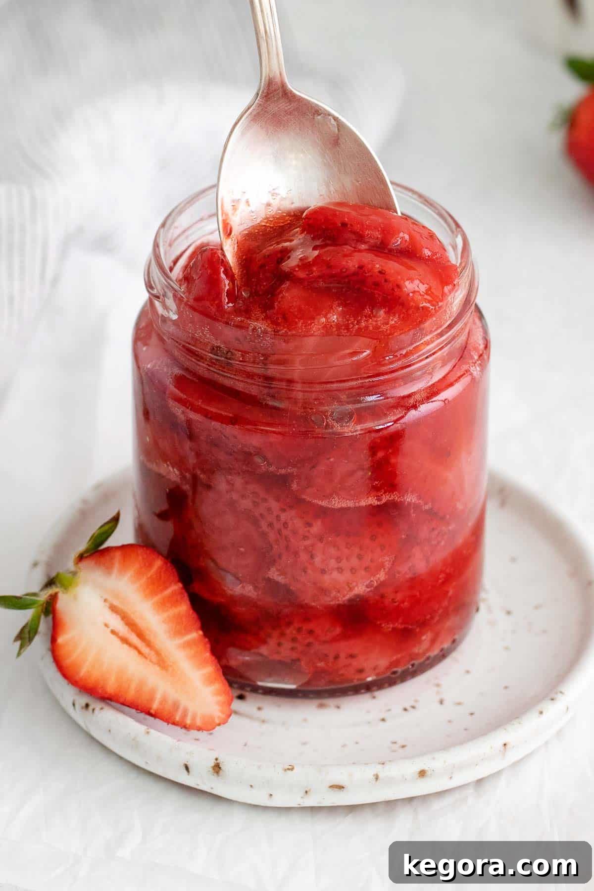 Luscious Strawberry Compote 6 A closeup of glistening strawberry compote in a clear glass jar, with a spoon nearby, emphasizing its fresh and homemade appeal