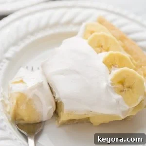 A generous slice of dairy-free banana cream pie on a white plate, showcasing its creamy layers.