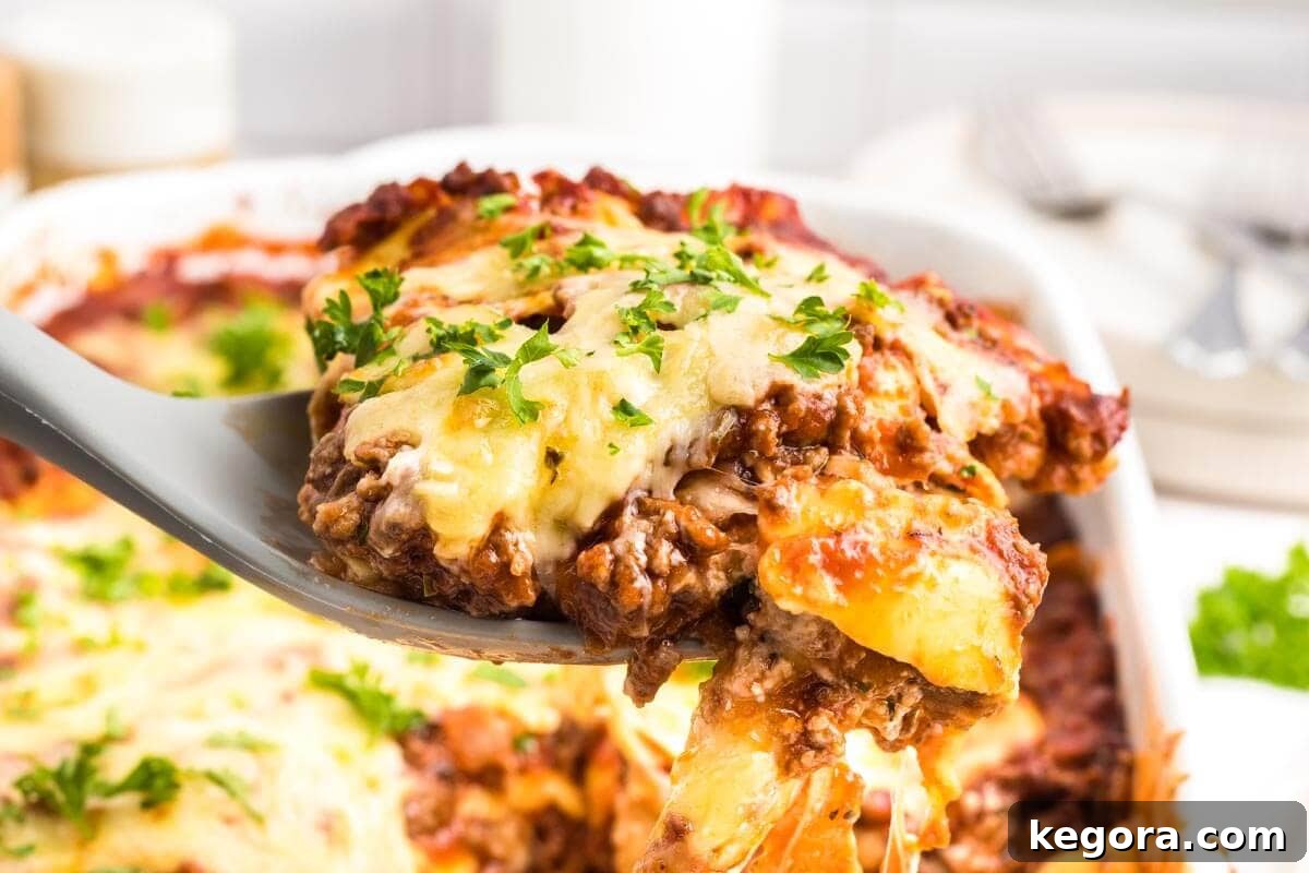 A serving spoon lifting a piece of Ravioli Lasagna with Meat Sauce.