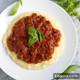 Chorizo Tomato Sauce topping polenta on a white plate garnished with basil