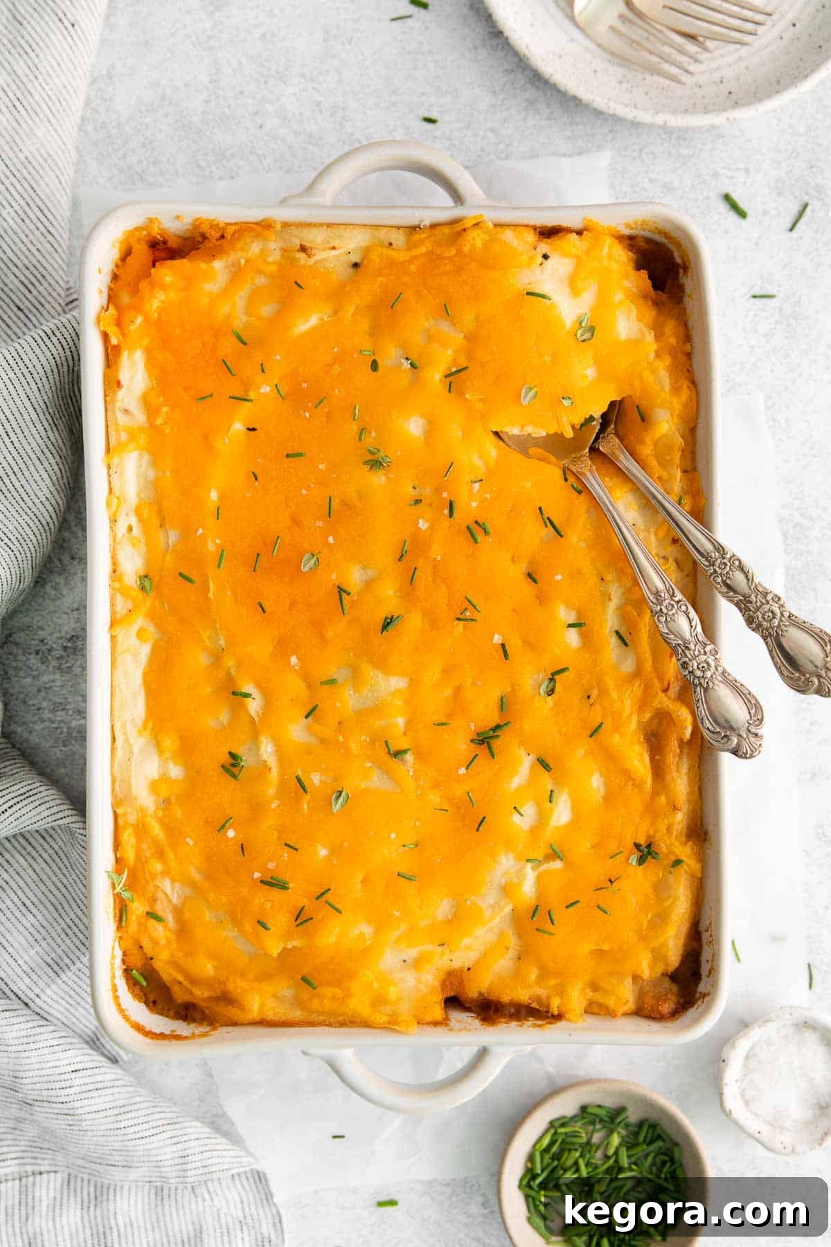 Hearty Gluten-Free Shepherds Pie 12 A baking dish filled with golden-brown gluten-free shepherd's pie, with two serving spoons resting inside, ready to be enjoyed.