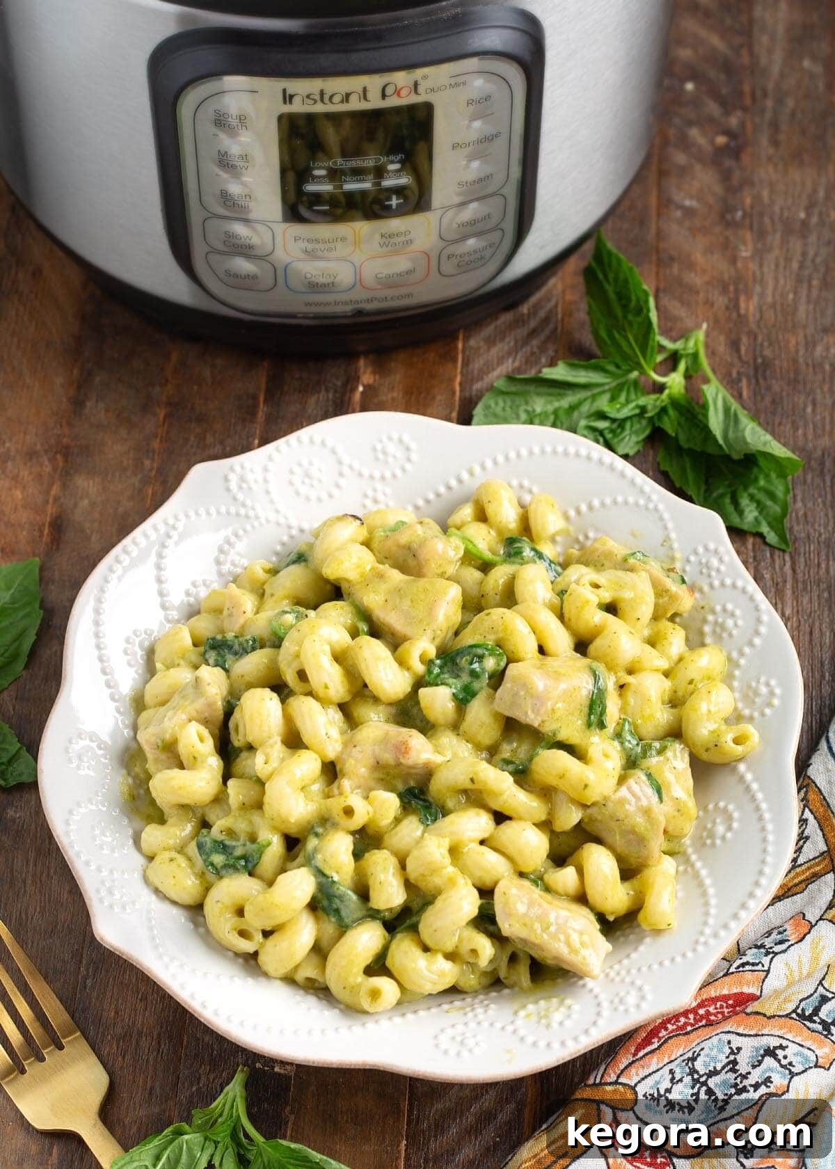 A beautifully presented white bowl of Instant Pot Chicken Pesto Pasta, with the Instant Pot visible in the soft-focus background.