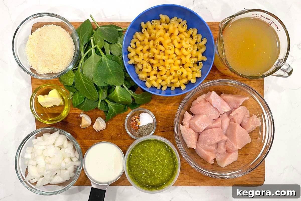 A spread of fresh ingredients for Instant Pot Chicken Pesto Pasta, including chicken, pasta, pesto, spinach, and spices.