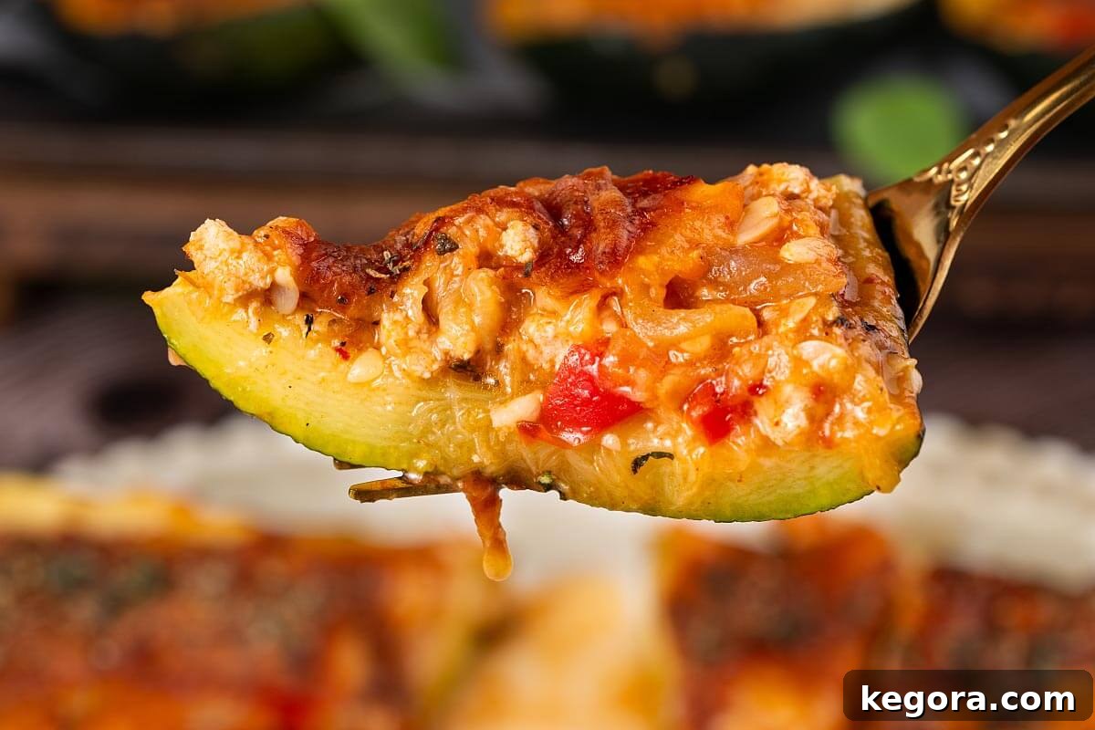 A fork taking a bite of a cheesy stuffed zucchini boat, highlighting the filling and melted cheese.