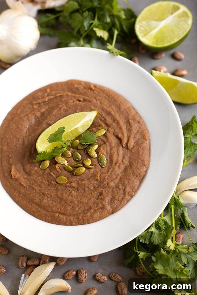 Creamy Homemade Slow Cooker Refried Beans 2 Refried Beans in a white bowl topped with papitas cilantro and lime