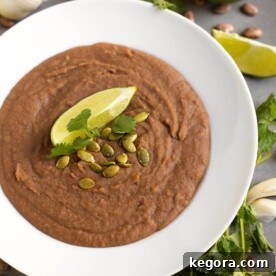 Creamy Homemade Slow Cooker Refried Beans 4 Refried Beans in a white bowl topped with papitas cilantro and lime