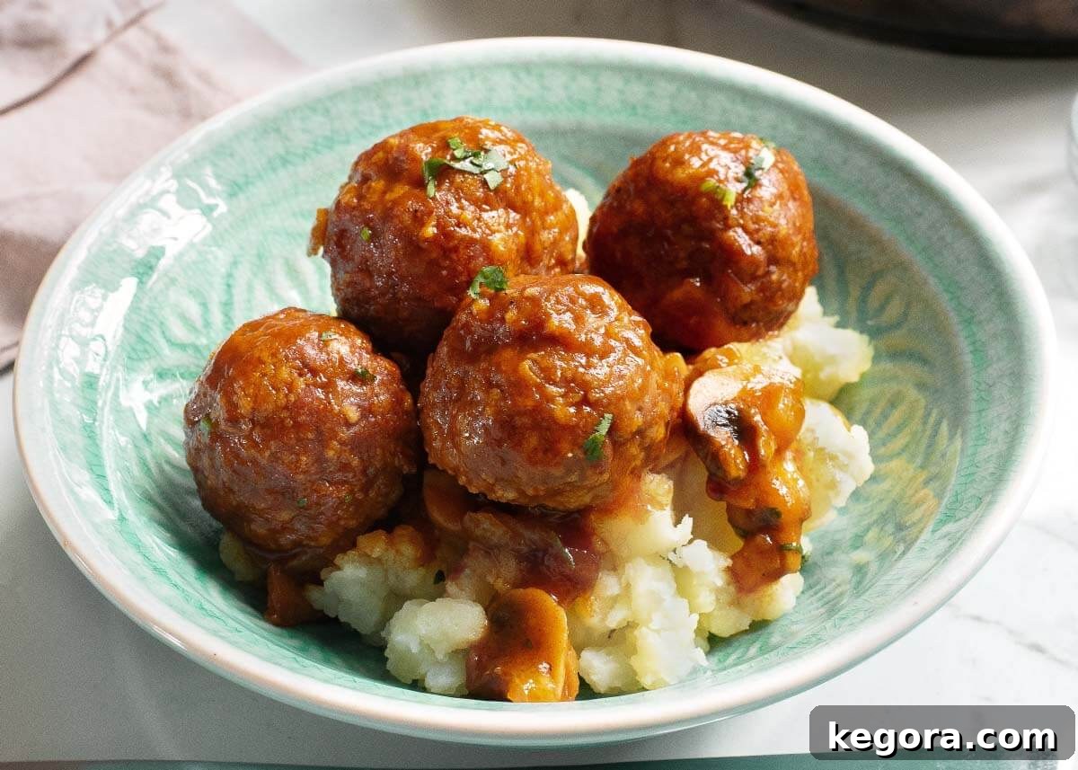 Classic Salisbury Steak Bites 3 Meatballs in a green bowl on a bed of mashed potatoes, garnished with fresh herbs.