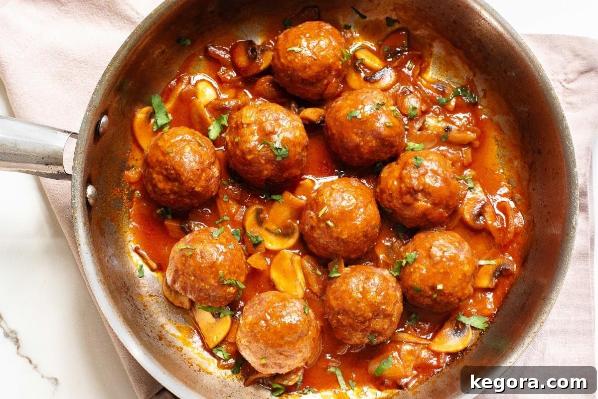 Classic Salisbury Steak Bites 8 Close-up of Salisbury Steak Meatballs and gravy in a skillet, garnished with fresh herbs.