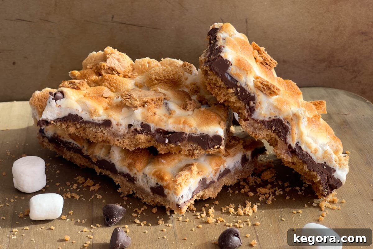 Ultimate Smores Bars 4 Three S'mores Bars stacked on a wooden board, showing off their distinct layers of crust, chocolate, and toasted marshmallow.