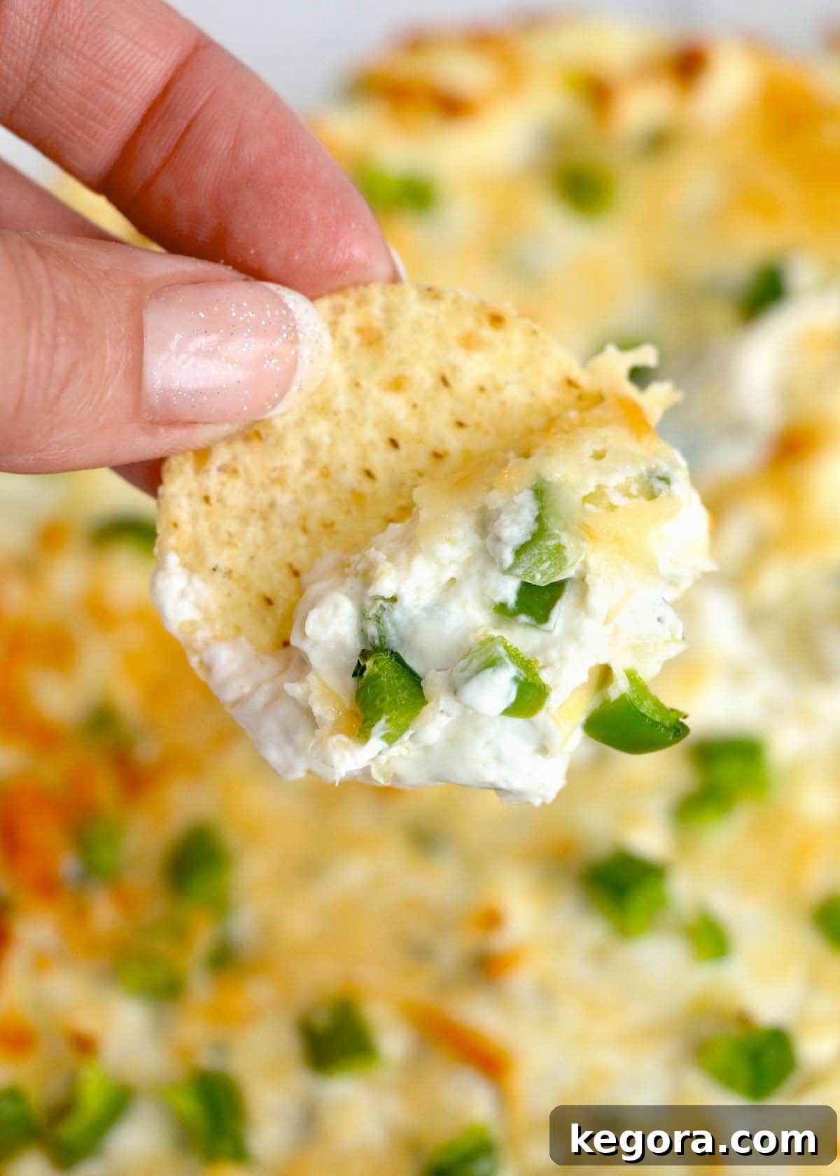 Hand reaching for a chip to dip into a bowl of creamy Baked Artichoke Jalapeño Dip.