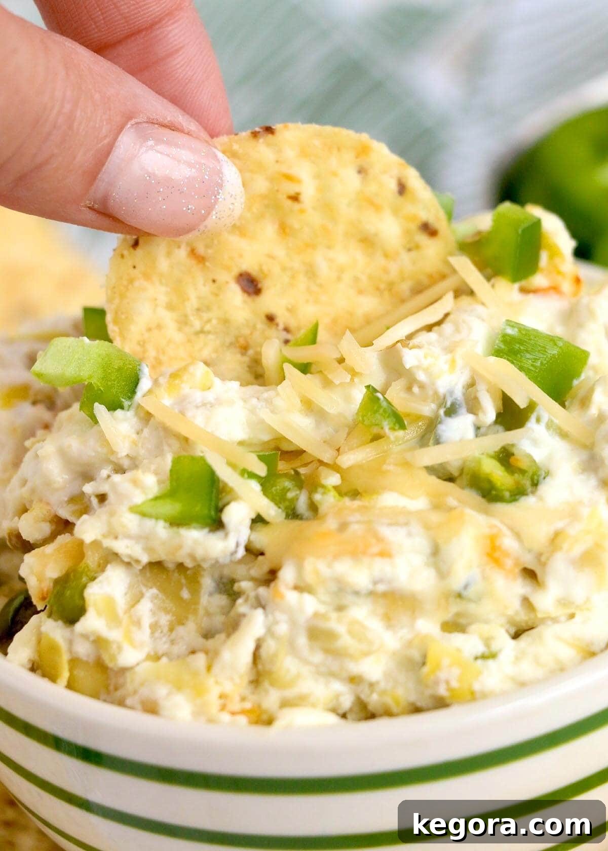 Close-up shot of a chip being dipped into a bowl of creamy, baked artichoke jalapeño dip, highlighting its enticing texture.