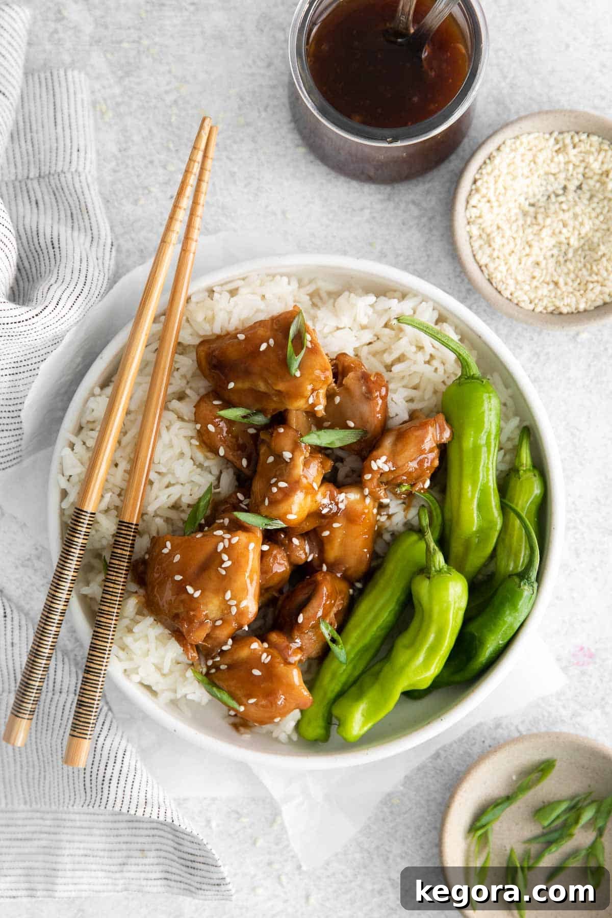 A bowl of chicken, rice, snap peas, and teriyaki sauce with chopsticks on the side
