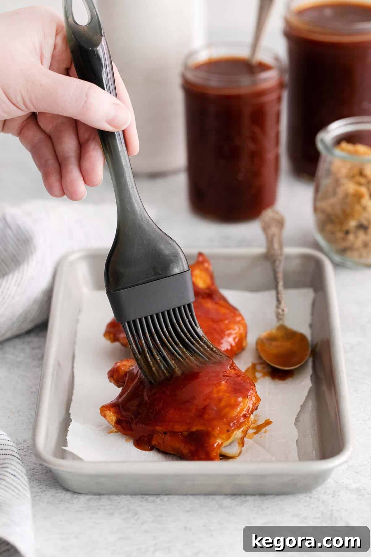 A hand basting a piece of chicken with gluten-free BBQ sauce