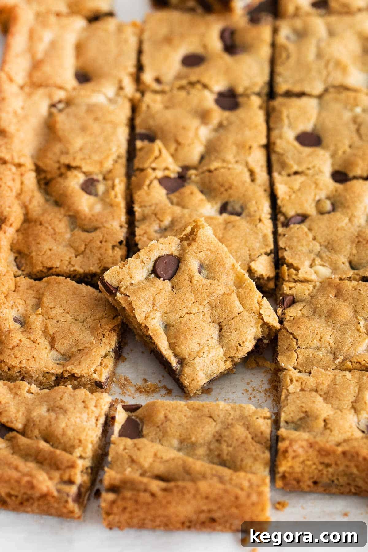 A close-up shot of golden gluten-free blondies neatly sliced in a baking pan, with one piece playfully placed on top, ready to be enjoyed.