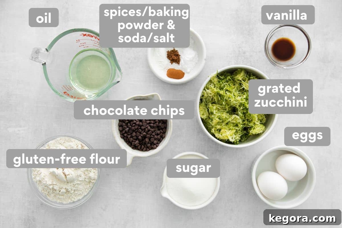 Overhead view of all the gluten-free zucchini muffin ingredients meticulously laid out on a clean white table, showcasing fresh zucchini, flour, eggs, and chocolate chips.