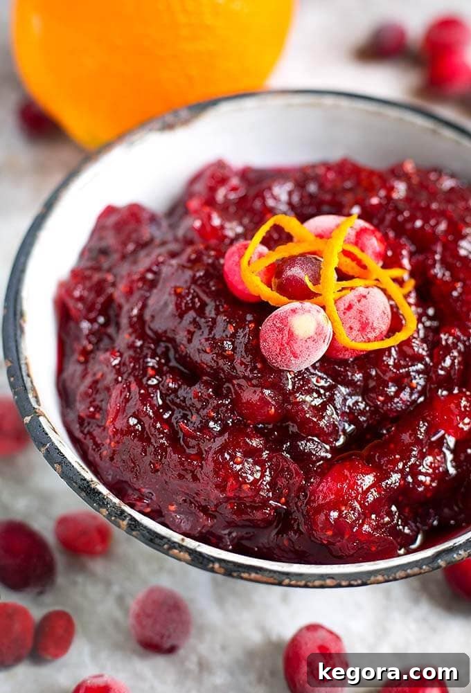 Effortless Instant Pot Cranberry Sauce 2 Cranberry Sauce in a white bowl with black rim surrounded by frosted cranberries