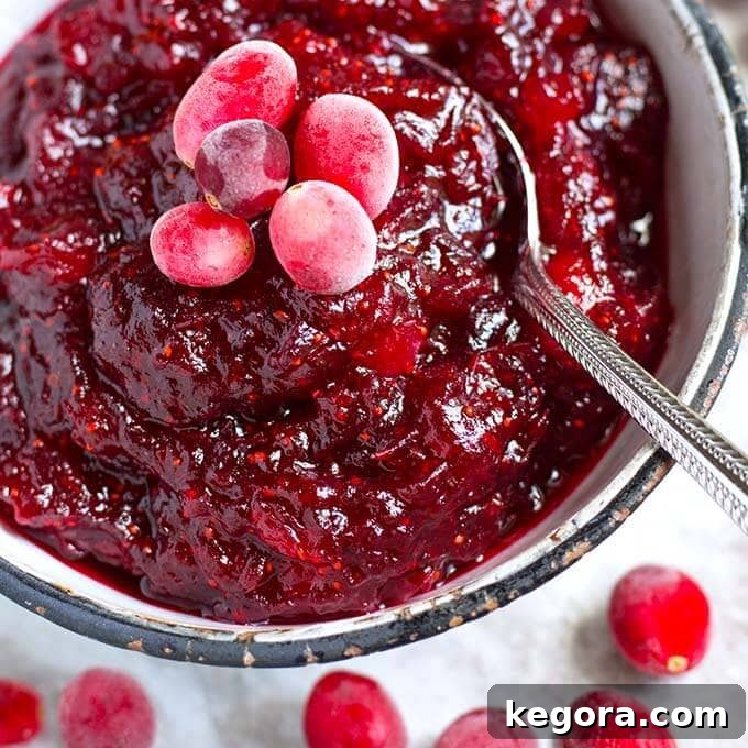 Effortless Instant Pot Cranberry Sauce 3 Cranberry Sauce in a white bowl with black rim surrounded by frosted cranberries and a spoon