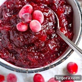 Effortless Instant Pot Cranberry Sauce 5 Cranberry Sauce in a white bowl with black rim surrounded by frosted cranberries and a spoon