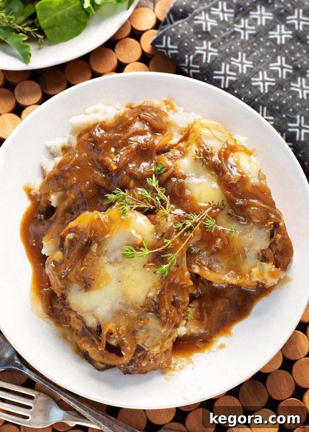 Slow Cooker French Onion Pork Chops and mashed potatoes on white plate, garnished with fresh thyme.