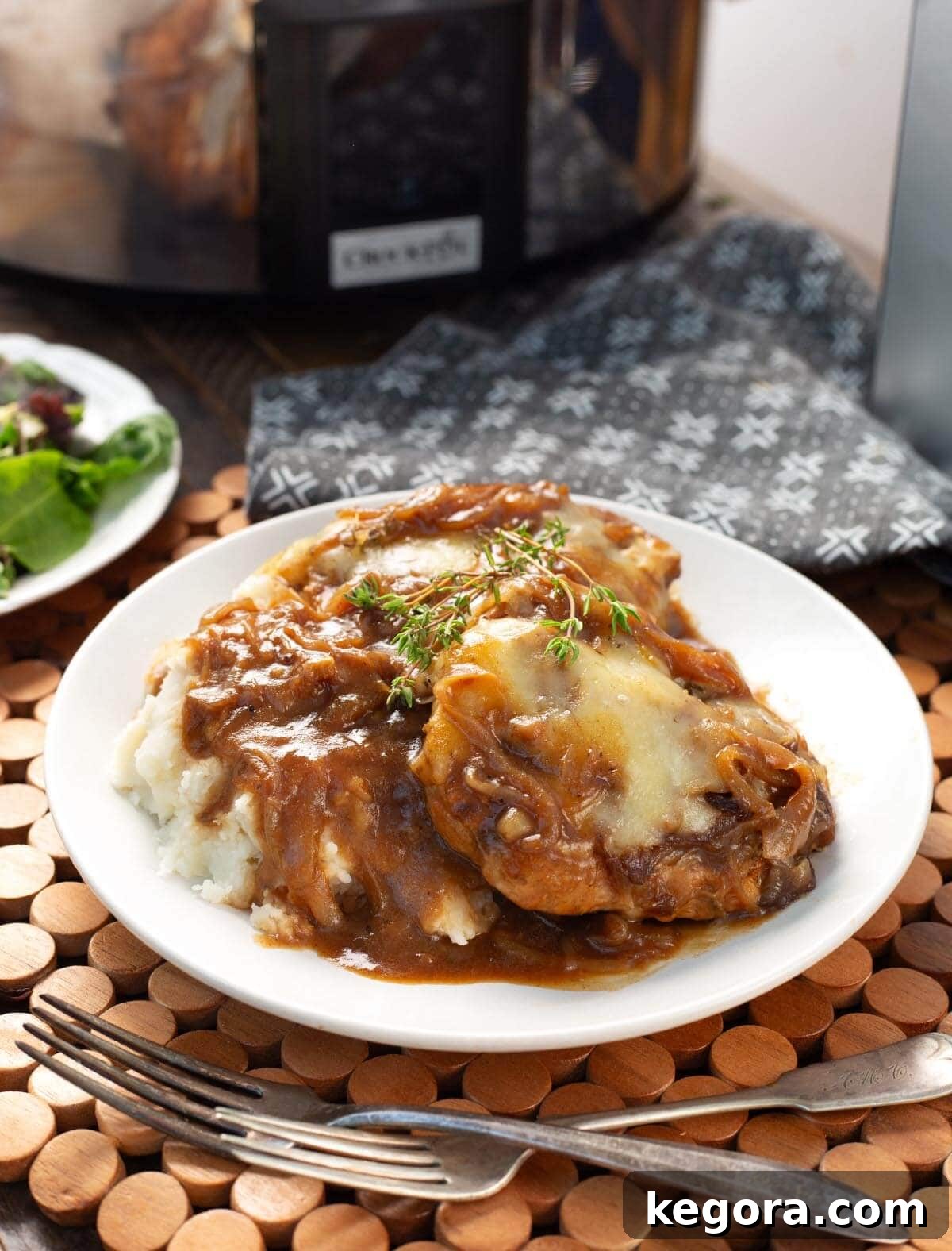 Slow Cooker French Onion Pork Chops served on a white plate with mashed potatoes and generous spoonfuls of gravy, garnished with fresh herbs.