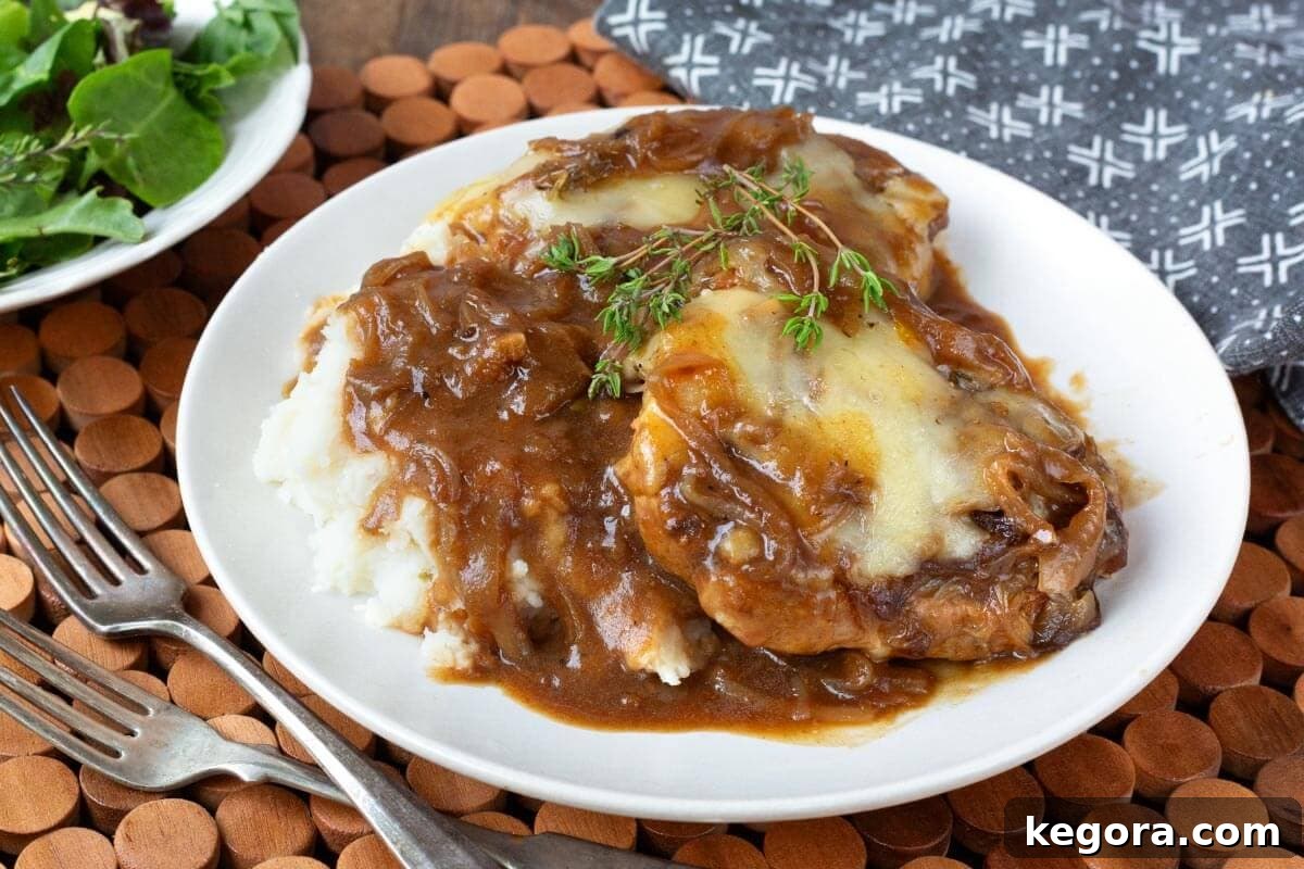 Close-up of Slow Cooker French Onion Pork Chops on a white plate with mashed potatoes.