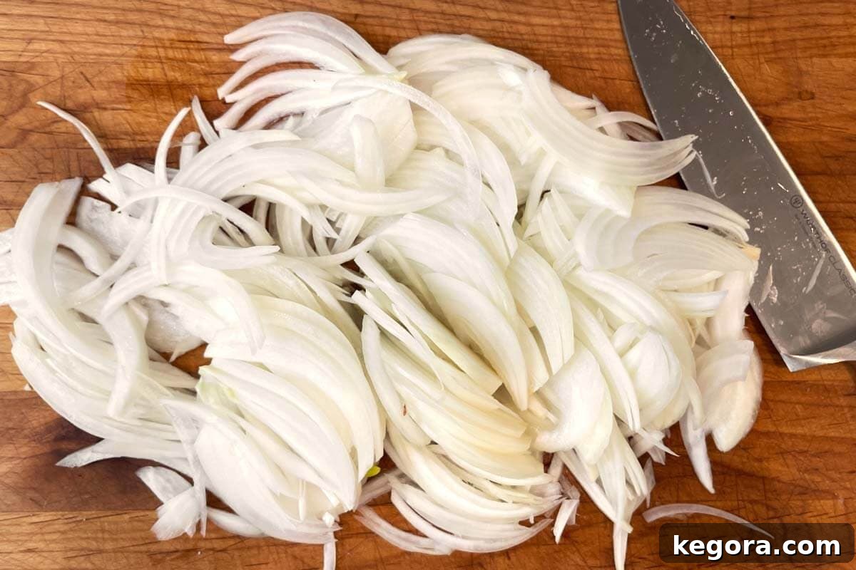 Thinly sliced yellow onions on a wooden cutting board, ready for caramelization.