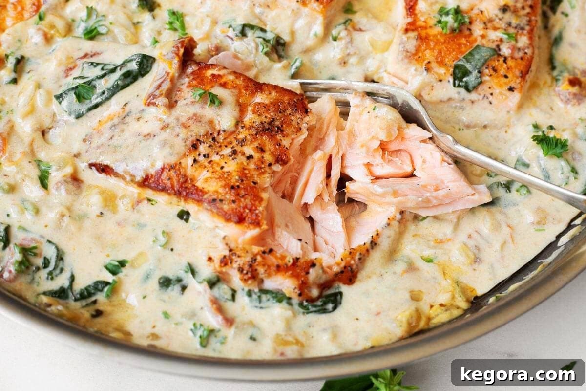 Decadent Creamy Garlic Tuscan Salmon 3 A fork breaking into a perfectly cooked salmon fillet, showcasing its flaky texture, in a pool of creamy Tuscan sauce.