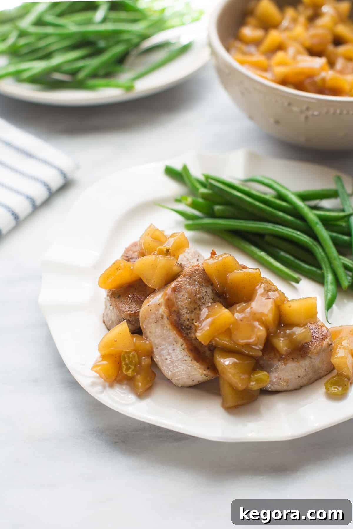 Pork tenderloin medallions served on a white plate with homemade applesauce and green beans on the side, highlighting a beautiful and delicious family dinner.