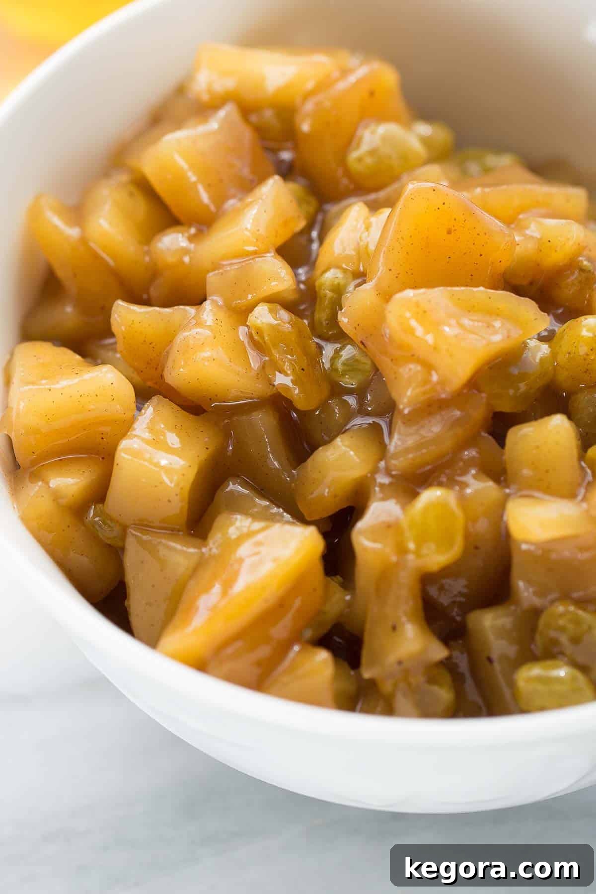 Close-up shot of homemade golden applesauce in a white bowl, showcasing its rich texture and inviting color, ready to be served.