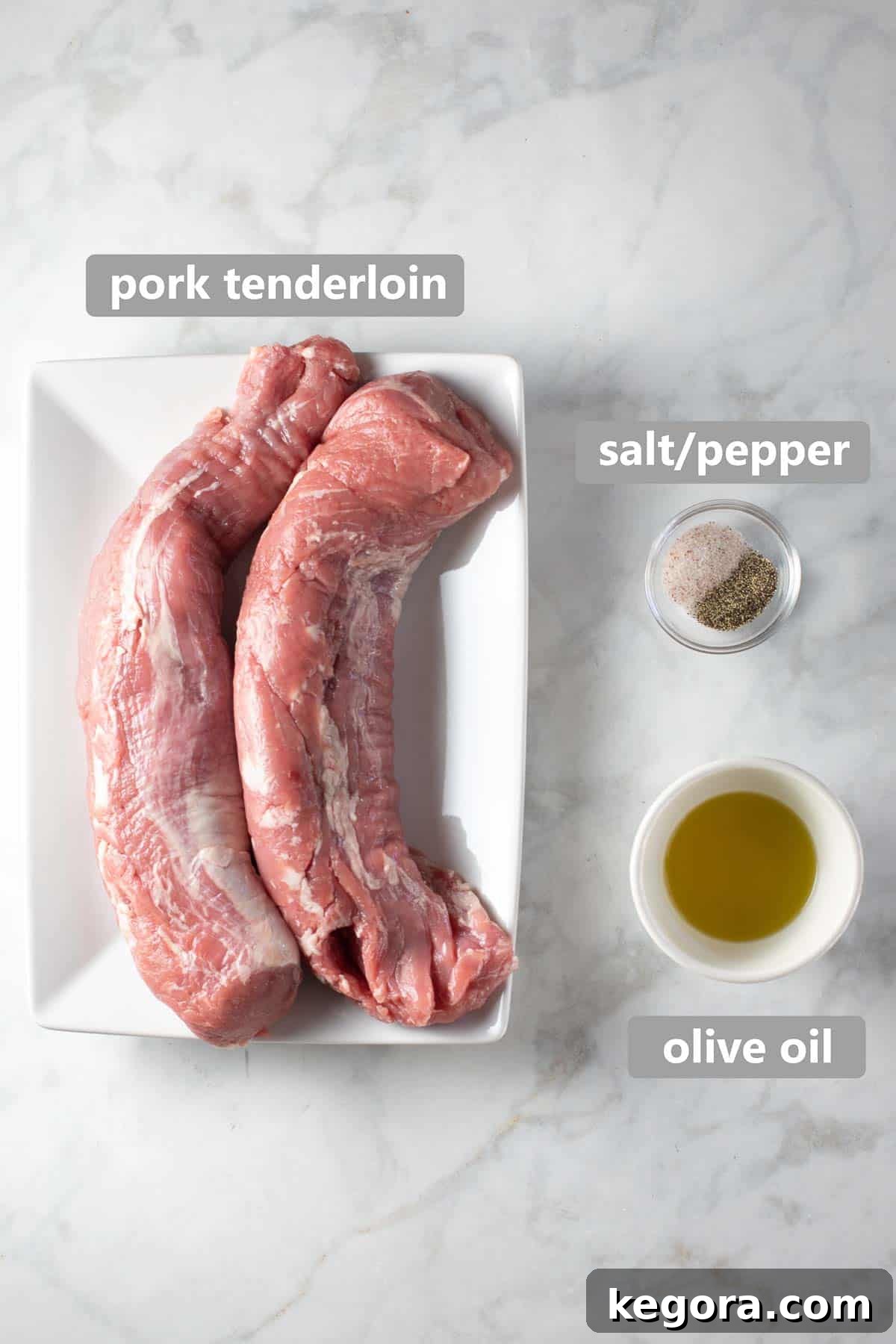 Overhead shot of raw pork tenderloin and olive oil on a marble background before cooking, indicating the fresh ingredients and simple preparation.