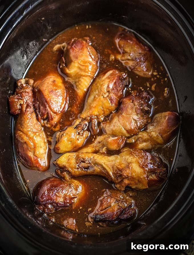 Sticky Chicken Drumsticks simmering in a black slow cooker, promising tender and flavorful results.