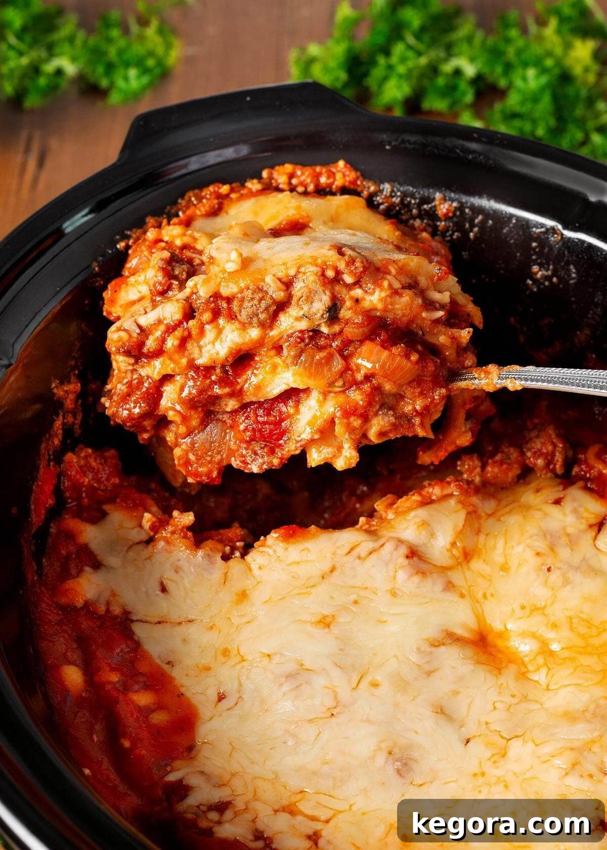 Slow Cooker Lasagna on a spoon in black crock.