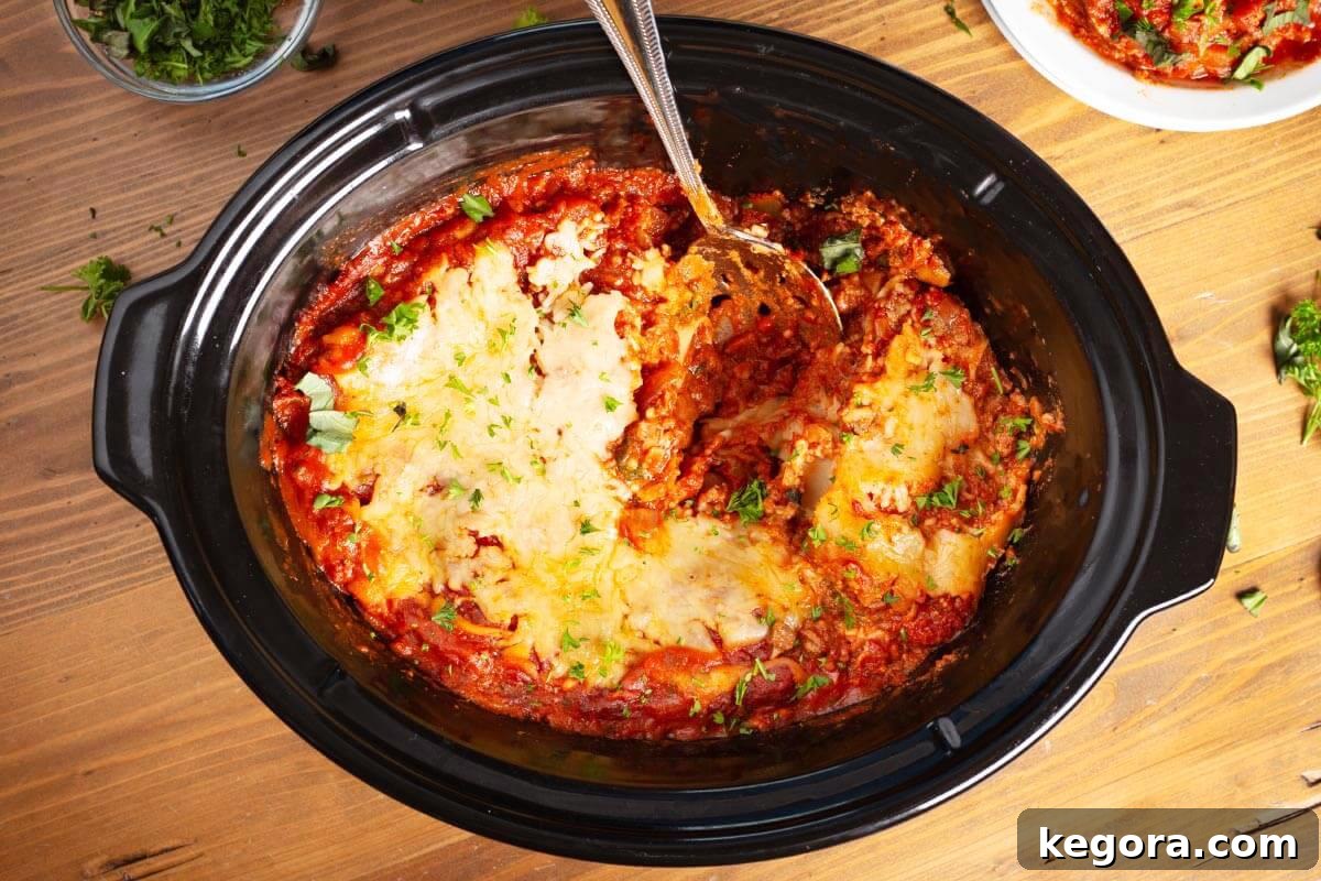 Slow Cooker Lasagna with a spoon in black crock.
