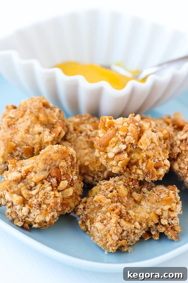 Golden brown gluten-free pretzel crusted chicken bites arranged neatly on a baking sheet with a side of a small bowl of dipping sauce.